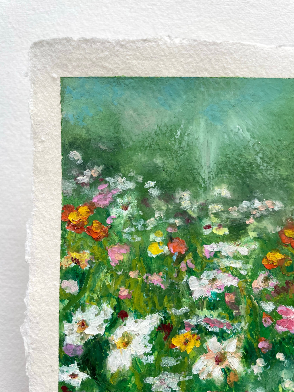 A close-up of a textured oil pastel painting depicting a lush green field filled with white, pink, yellow, and orange wildflowers, on a white textured paper.