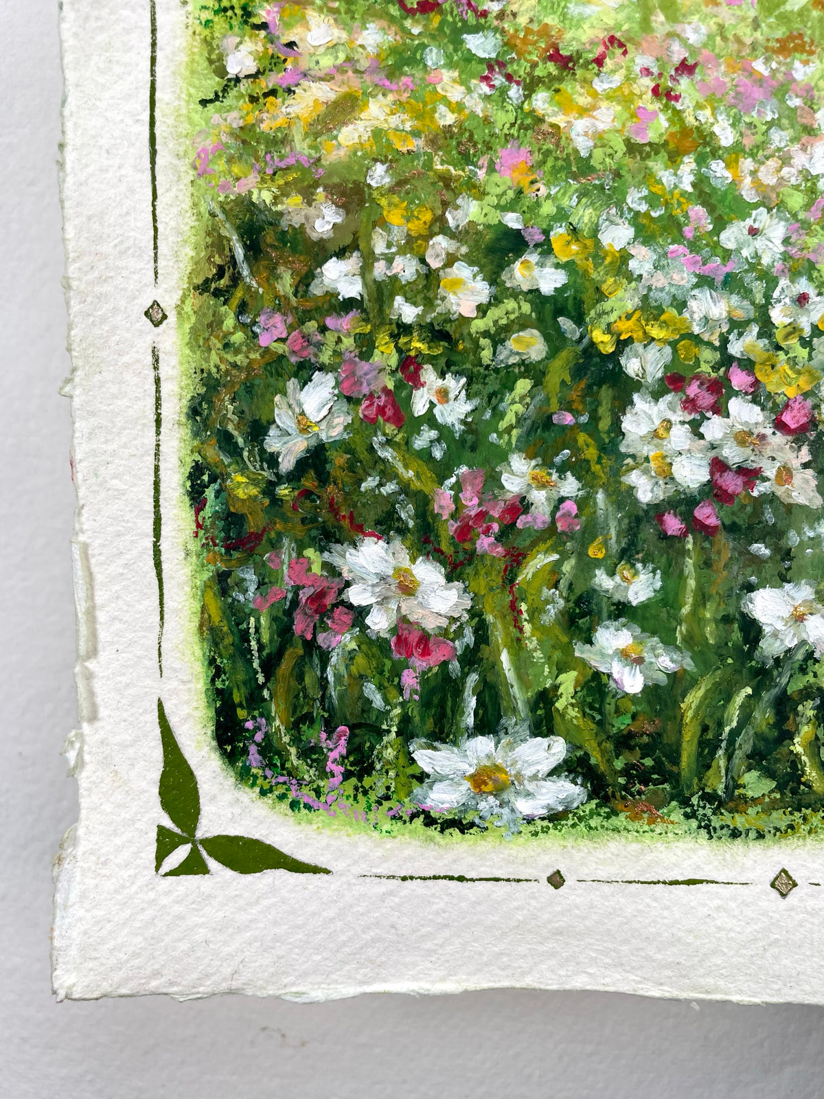 Close-up of an oil pastel painting on textured paper, showing a dense field of white, pink, yellow, and green wildflowers with a decorative white border and green corner accents.