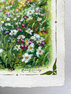A close-up of an oil pastel painting on textured white paper, depicting a dense cluster of white, pink, and yellow wildflowers with green foliage. The artist's signature is visible near the bottom, and a green geometric corner motif is printed in the lower corner.