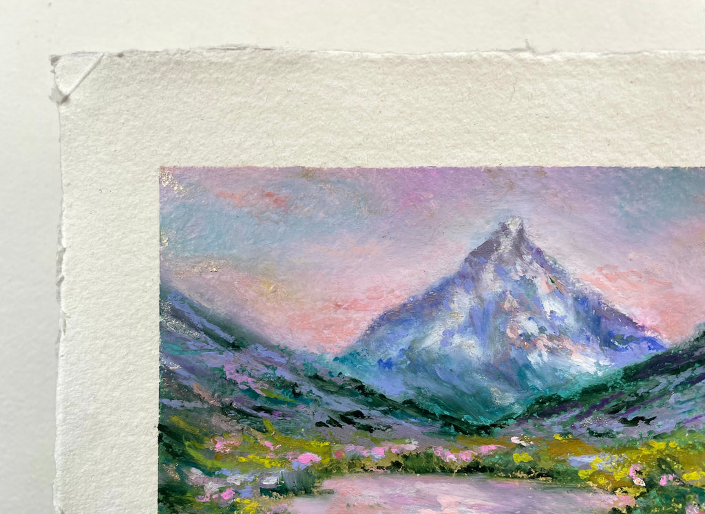 A close-up of an oil pastel painting on paper featuring an impressionistic landscape painting of a mountain peak under a pink and purple sky.