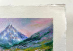 A close-up of a textured painting on paper featuring an impressionistic landscape painting of a mountain range under a pink and purple sky.
