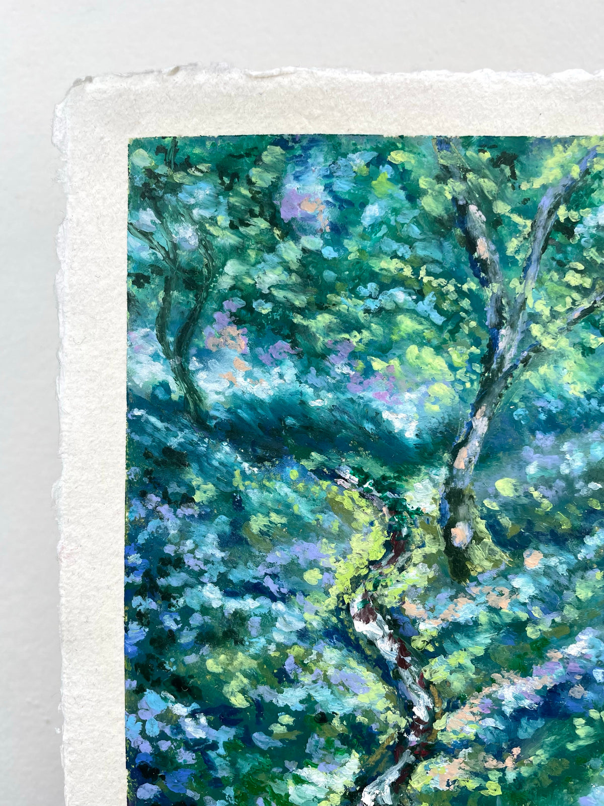 A close-up of a textured oil pastel painting depicting a lush green forest with dappled sunlight and purple-blue floral accents, printed on white handmade paper with a visible deckled edge.