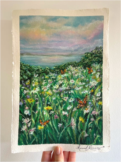 Original whimsical oil pastel wildflower landscape painting held in hand, featuring dreamy meadow scenery, soft atmospheric light, and peaceful impressionist textures.
