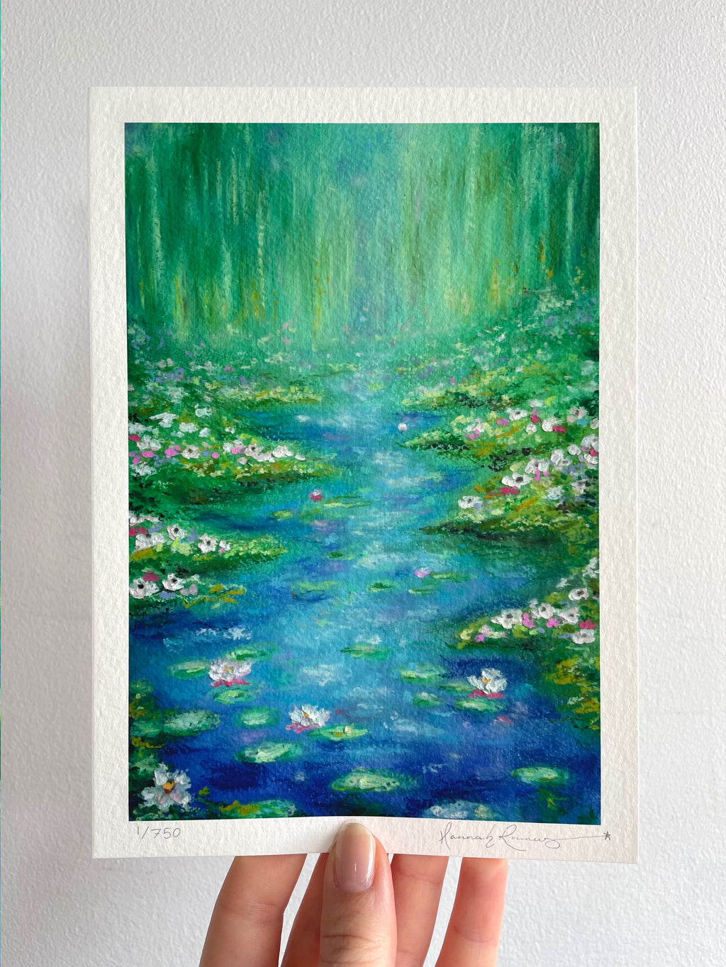 Giclée fine art print of original oil pastel impressionist landscape ‘Lighter Than The Lilies’ held against a white wall, featuring a magical pond landscape with water lilies, lily pads, wildflowers, soft weeping willow trees, sparkling sunlight and dreamy turquoise blue and green tones.