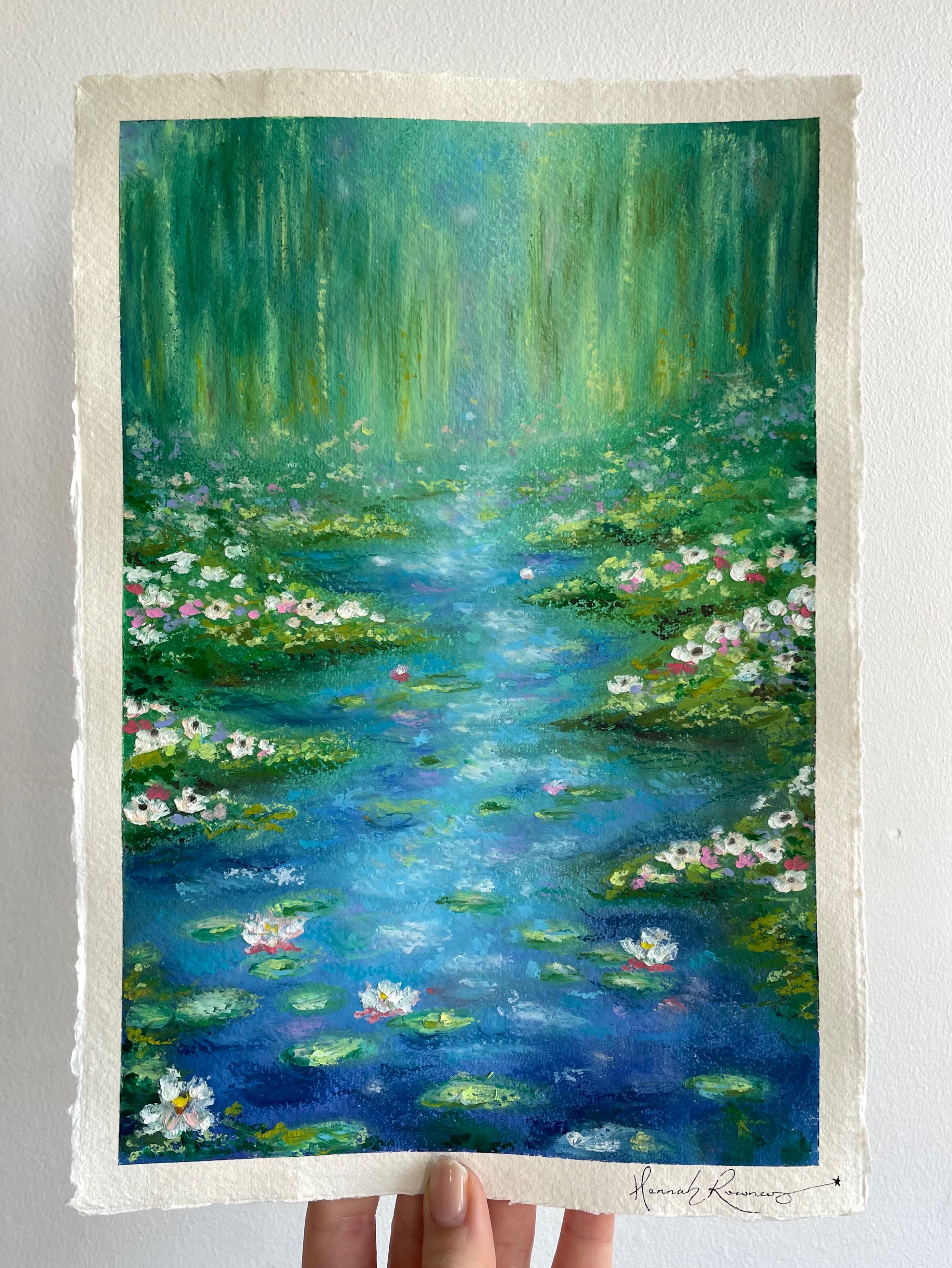 Original oil pastel impressionist painting ‘Lighter Than The Lilies’ held against a white wall, featuring a magical pond landscape with water lilies, lily pads, wildflowers, soft weeping willow trees, sparkling sunlight and dreamy turquoise blue and green tones.