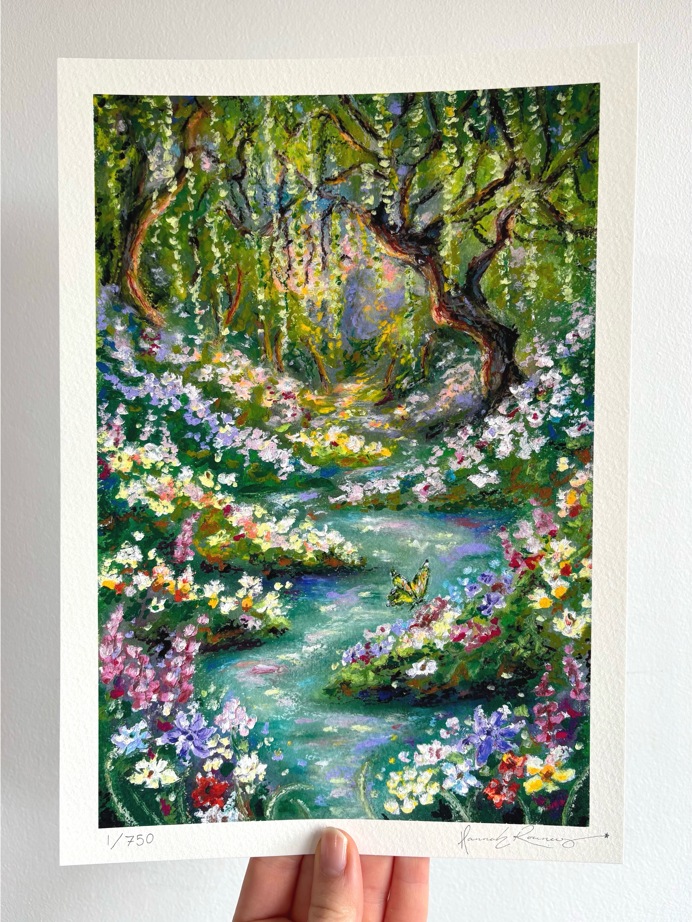 Limited edition giclée fine art print of whimsical oil pastel landscape “Looking for Wonderland,” featuring enchanted river, butterfly, wildflowers, and glowing weeping willow held against a white wall.