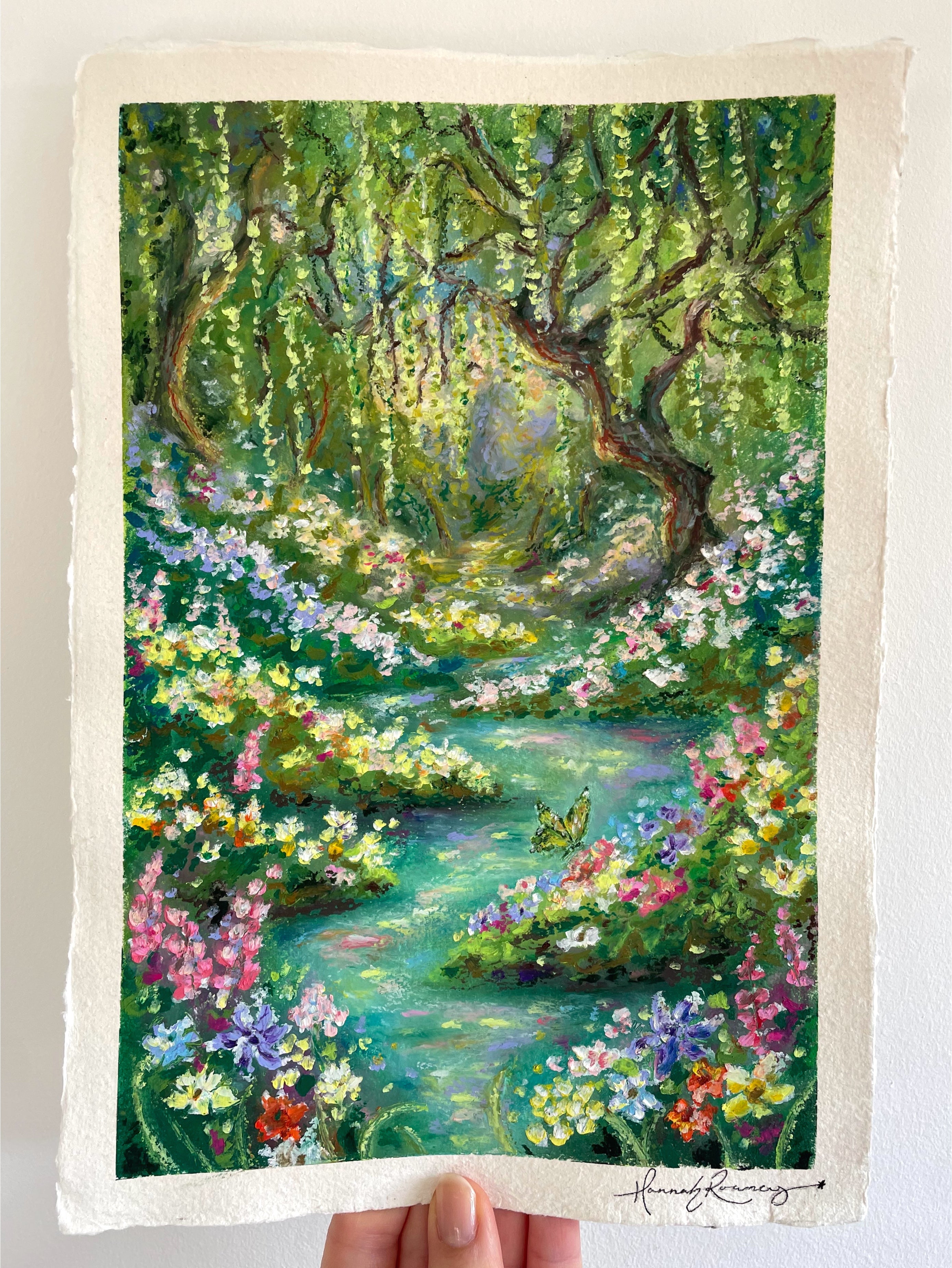 Original whimsical oil pastel landscape painting held in hand, featuring enchanted river, butterfly, colourful wildflowers, and ancient weeping willow in a magical layered forest scene.