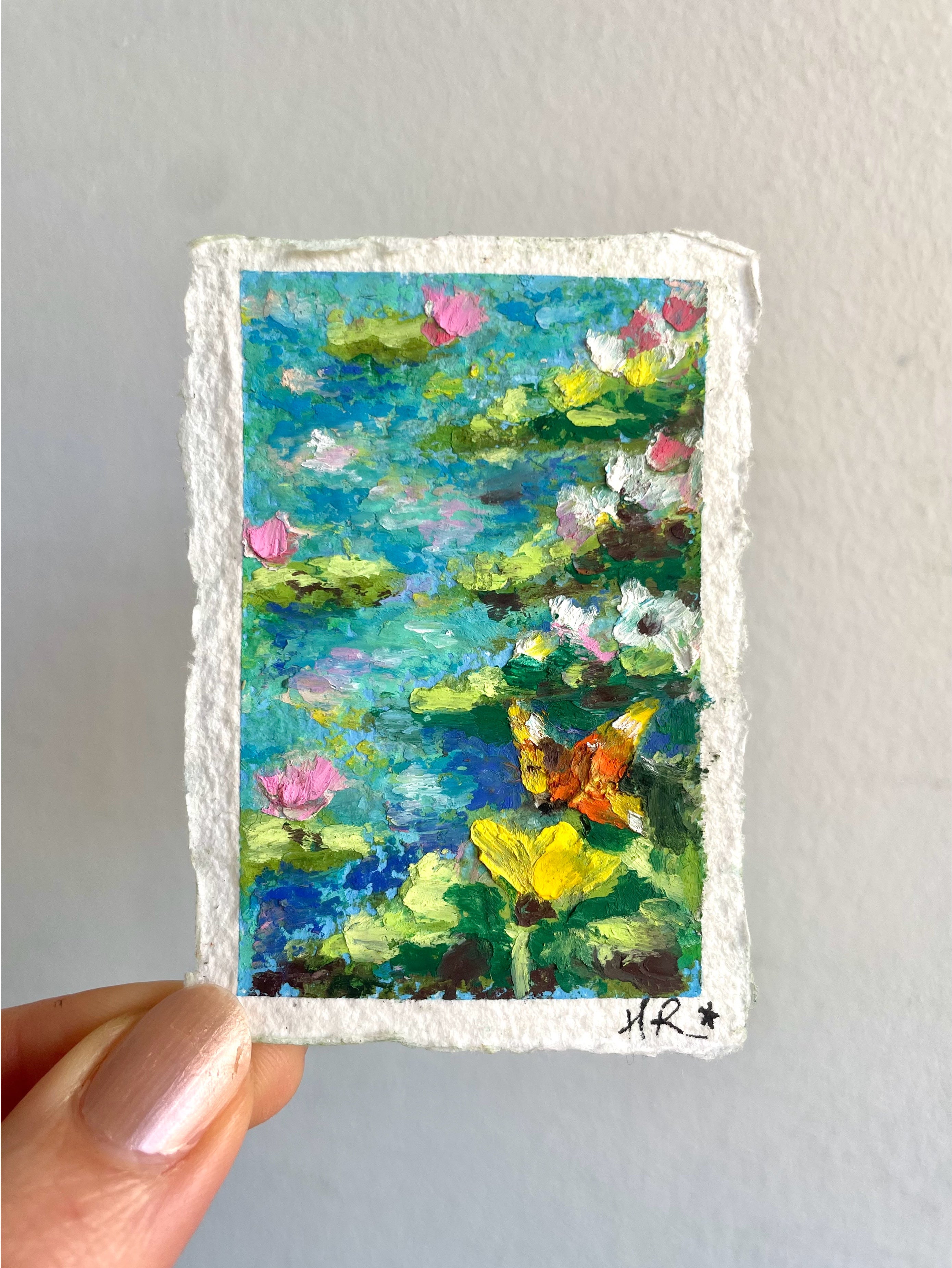 Close-up mini oil pastel pond painting showing mossy rocks, butterfly resting on wildflowers, and water lilies along a peaceful pond edge.