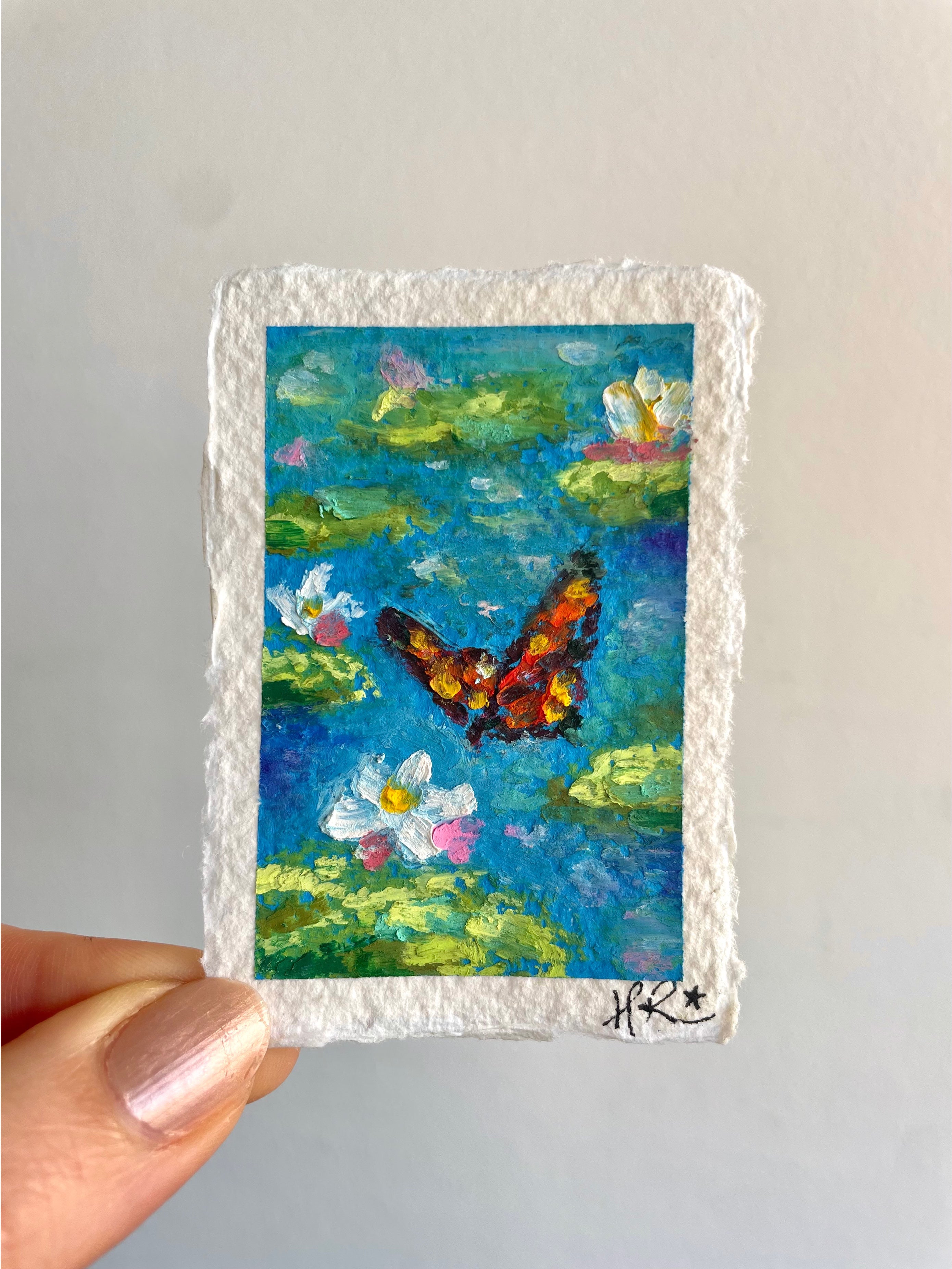 Whimsical mini oil pastel pond painting featuring vibrant orange butterfly above a blue pond with lily pads and blooming water lilies.
