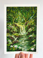 Limited edition giclée fine art print of enchanted Celtic-inspired forest with fairies, waterfalls, moss, and ancient trees held against a white wall.