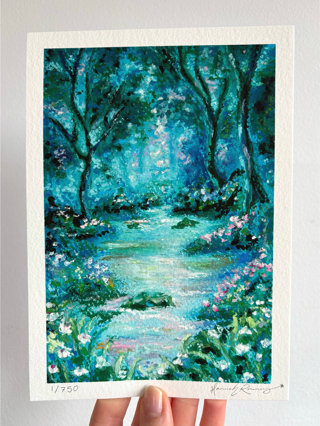 Limited edition hand-signed giclée fine art print of glowing mystical forest landscape with river, wildflowers, and ancient trees held against a white wall.