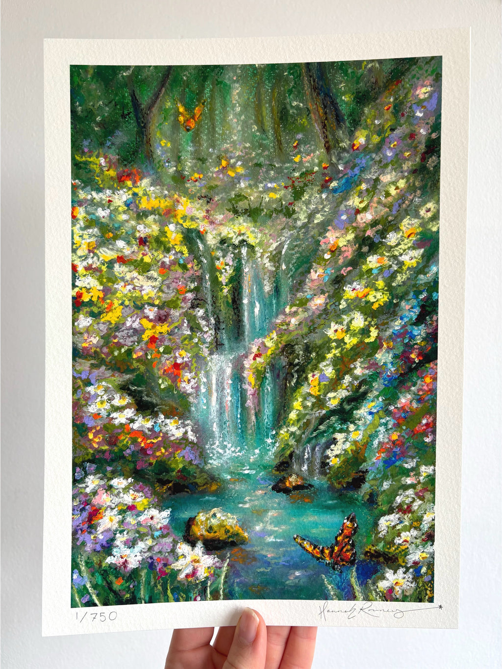 Limited edition giclée fine art print of magical fairytale forest landscape with waterfall, butterflies, wildflowers, and turquoise river held against a white wall.