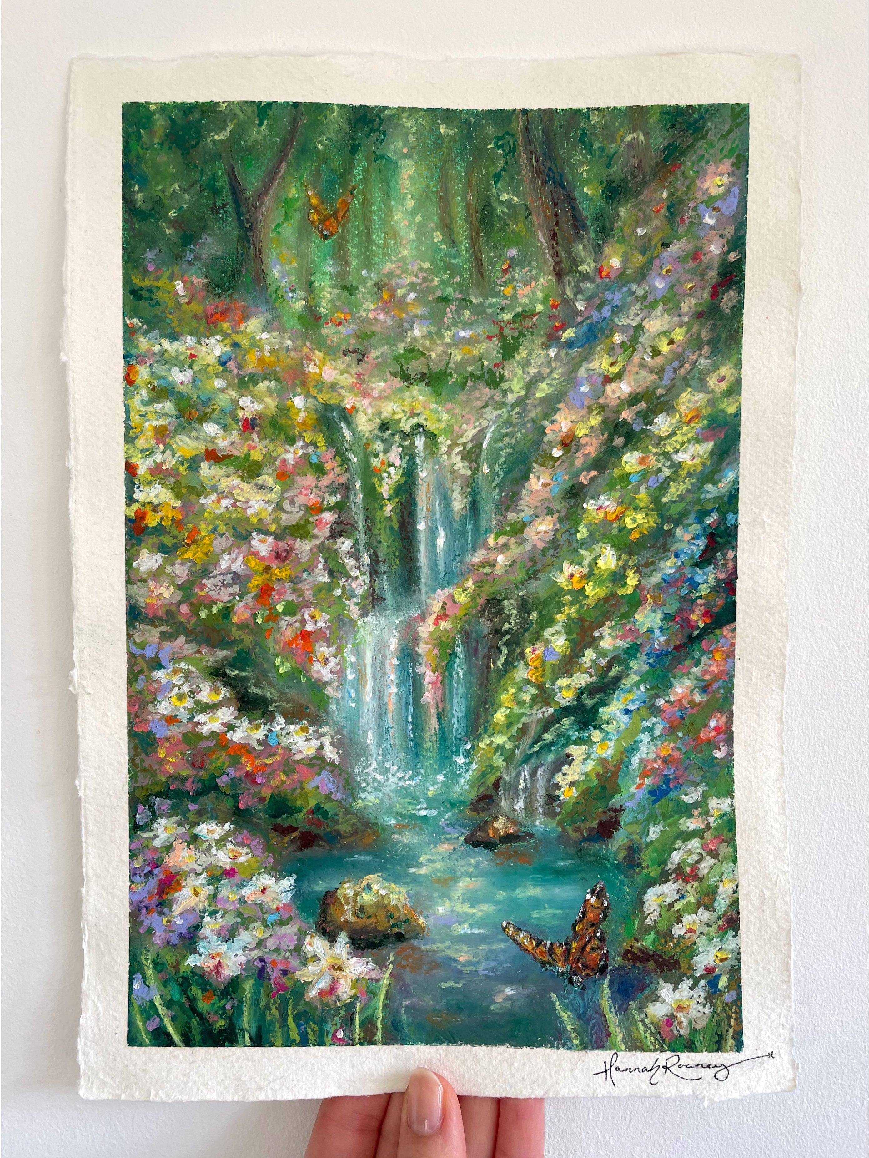 Original oil pastel fairytale forest painting held in hand, featuring magical waterfall, butterflies, turquoise water, ancient trees, and richly textured wildflowers.