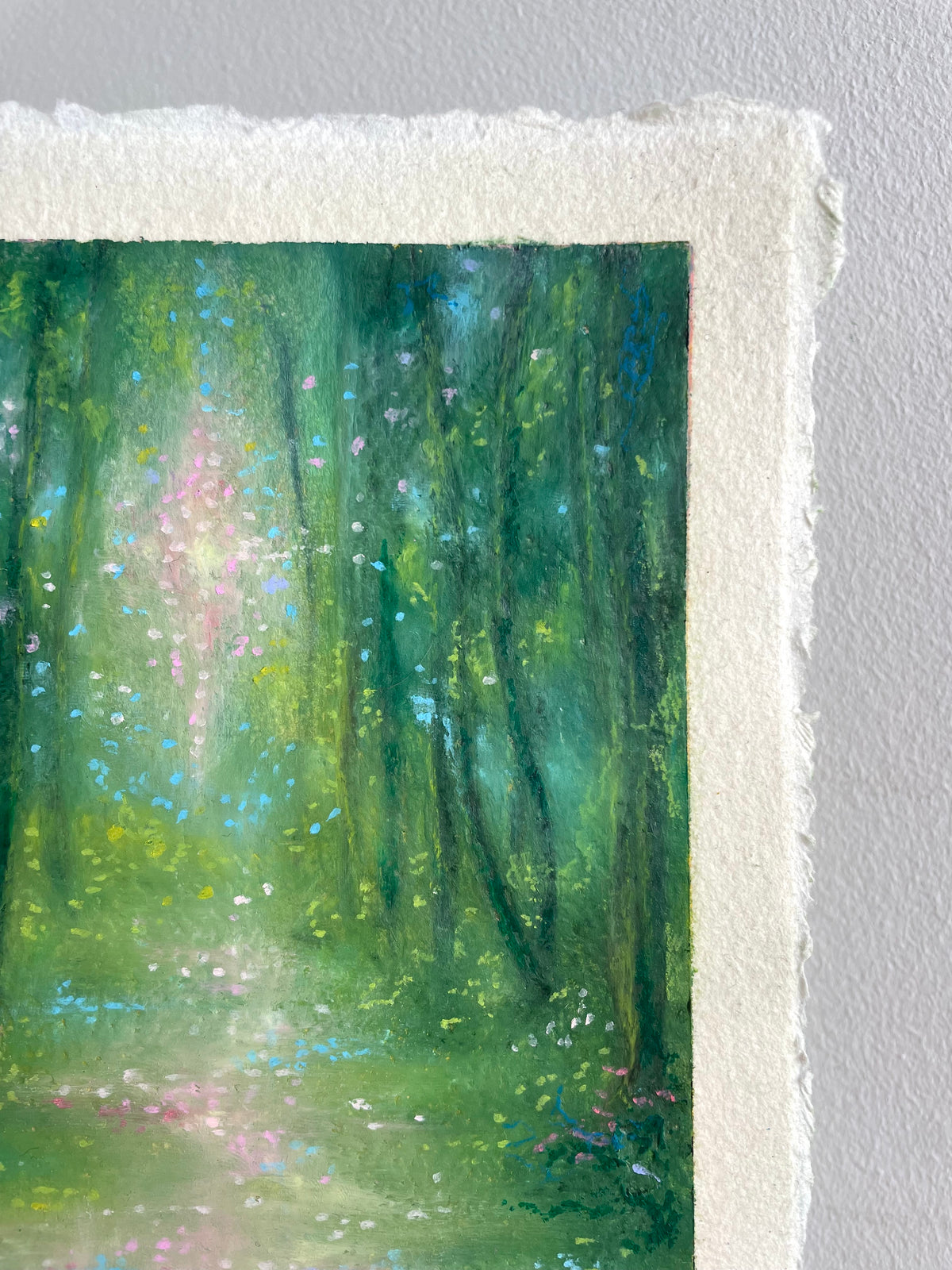 A close-up of an oil pastel painting on textured white paper, showing a forest scene with green and blue tones and a soft pink light.