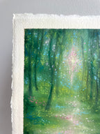 A close-up of an oil pastel painting on textured white paper, showing a forest scene with green trees, a soft light beam, and small pink and blue floral accents.