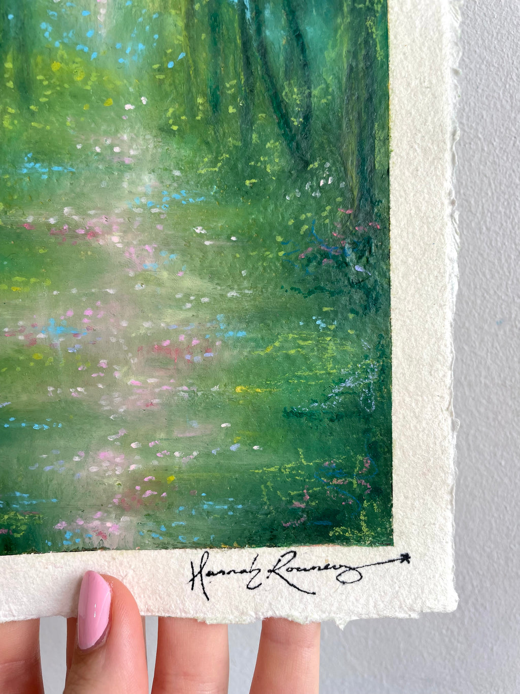 A close-up of an original painting featuring a green forest scene with a white border and a signature at the bottom.