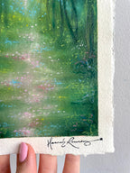 A close-up of an original painting featuring a green forest scene with a white border and a signature at the bottom.