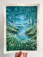 Whimsical oil pastel landscape painting held in hand, featuring an enchanted forest with flowing stream, wildflowers, and magical nature scenery against a white background.