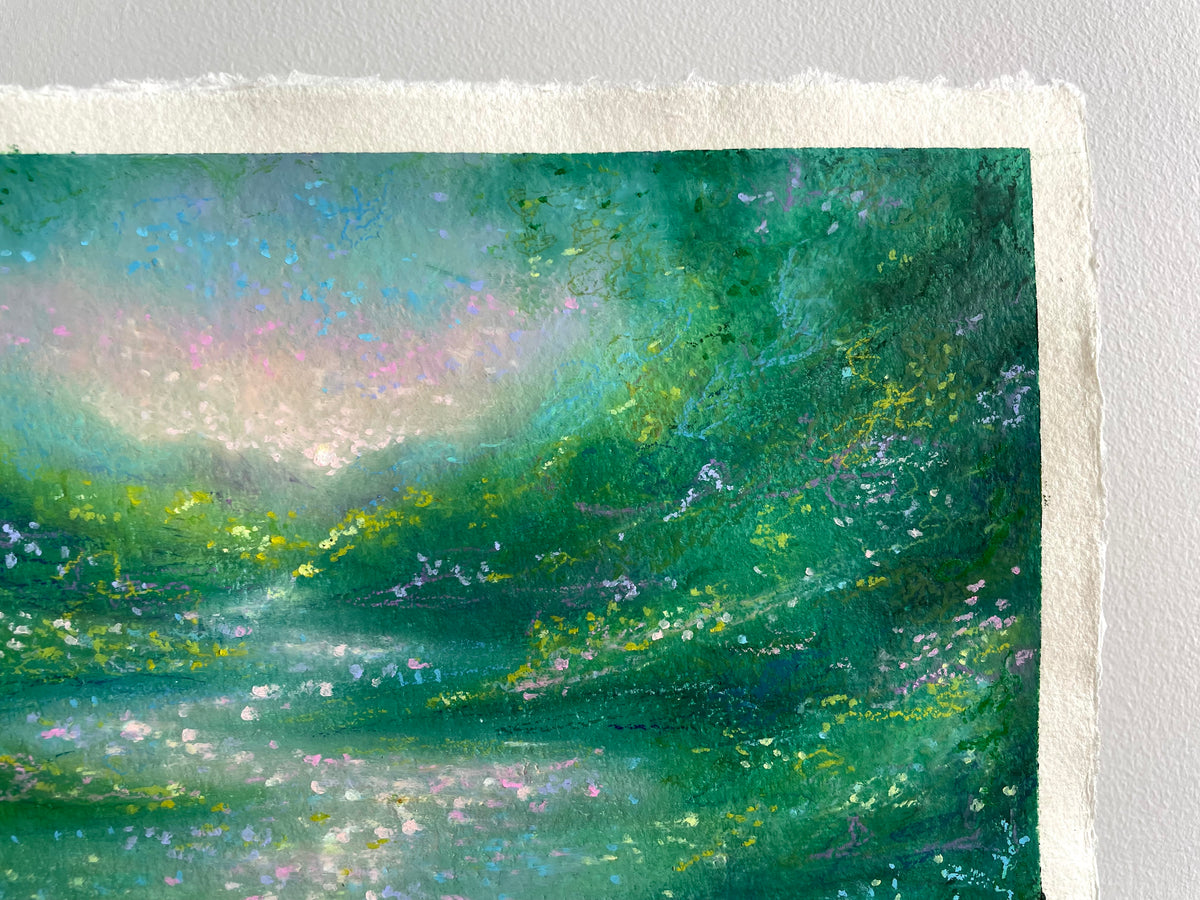 A close-up of a textured oil pastel painting on handmade paper, depicting a lush green landscape with soft pink and blue sky tones, finished with a white deckled-edge border.